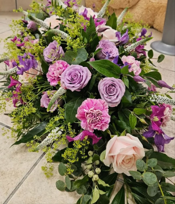 Funeral spray arrangement with purple roses and carnations