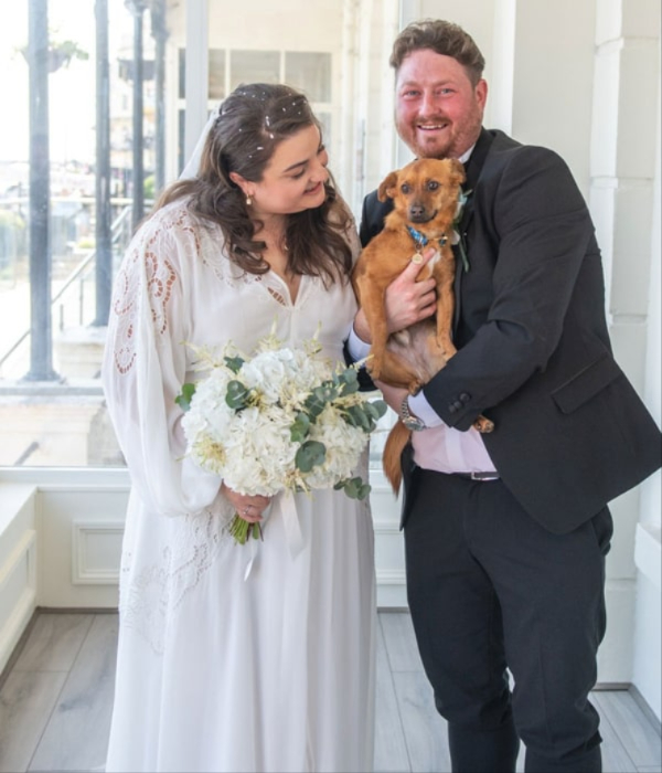 Bride and groom holding bouquet of white wedding flowers with their dog